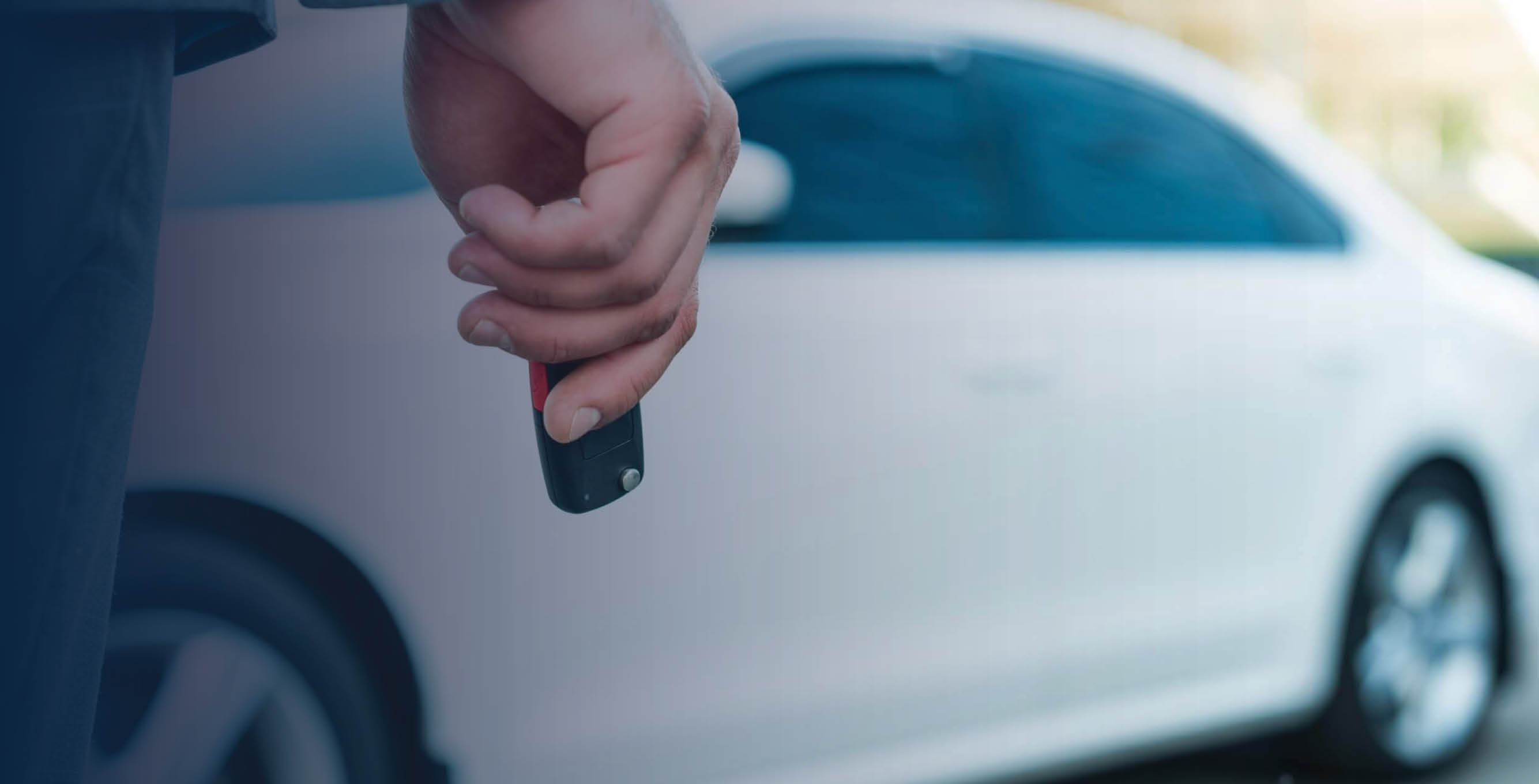 Hand holding car key in front of white car.