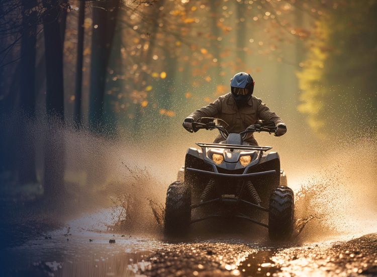 ATV being driven through a mud puddle in a forest.