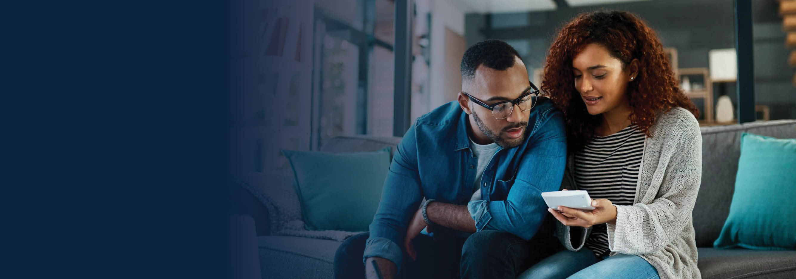 Couple looking at device while sitting on sofa.